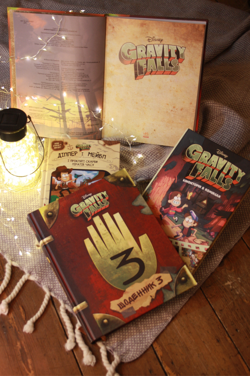 Gravity Falls books arranged with warm string lights